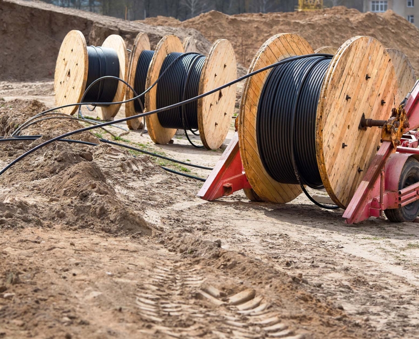 Several wooden coils with power cable laid in trench. Concept of electricity supply for construction projects_